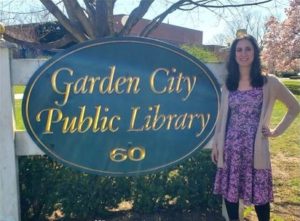 photo of Young Adult Librarian next to Garden City Public Library sign on lawn